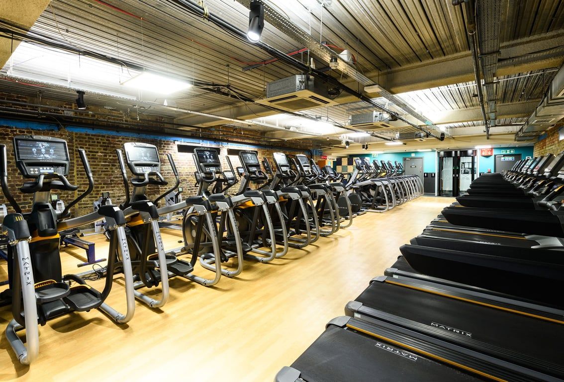 PureGym London Tower Hill: Rows of treadmills and exercise bikes in a dimly lit gym interior with exposed ceiling.