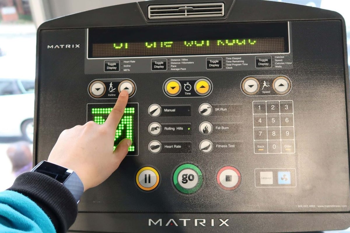 Hand pressing incline up button on treadmill control panel with various settings and butto