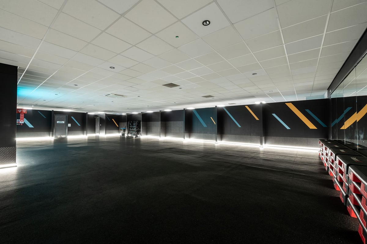 PureGym Birmingham Beaufort Park: Fitness class studio with rubber flooring and step platforms next to a mirrored wall.