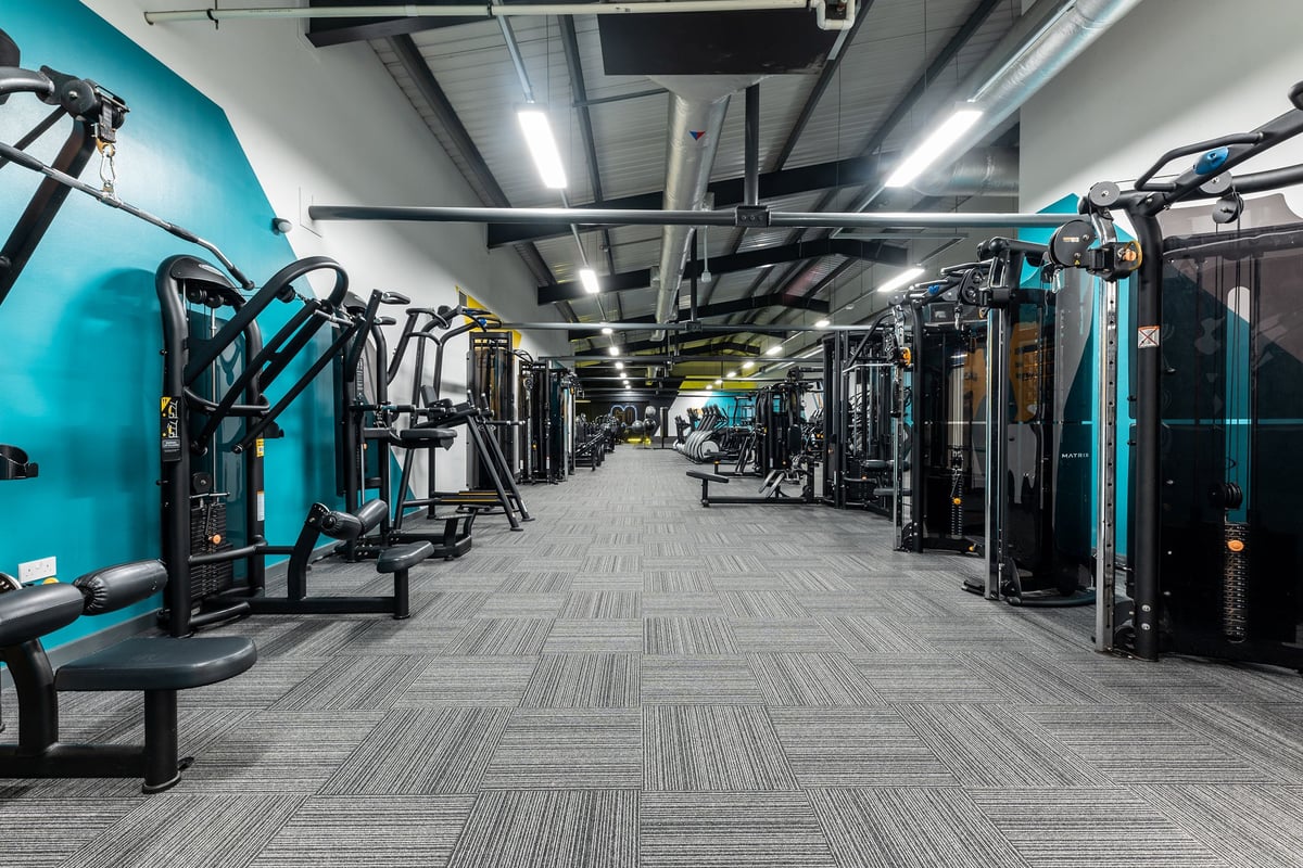 PureGym Ashton Under Lyne: Rows of resistance machines, benches, turquoise equipment, and industrial ceiling fixtures.