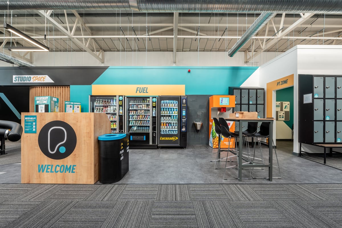 PureGym Bridgend: Fuel vending machines, snack area with high stools and tables, studio welcome sign.