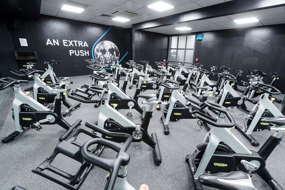 PureGym Billericay: Rows of stationary bikes in a dimly lit studio with motivational slogan on wall.