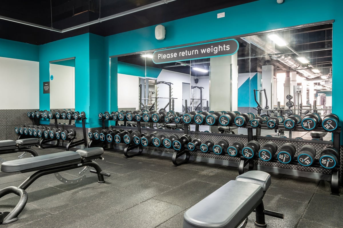 PureGym Manchester Market Street: Rows of dumbbell racks, weight benches and a sign requesting weights be returned.