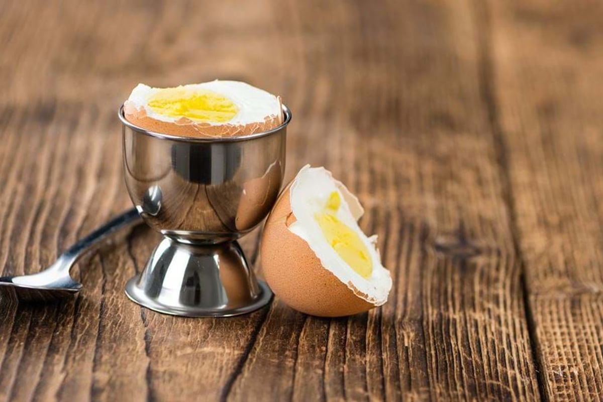 Soft boiled egg in a metal egg cup with a spoon on a wooden surface.