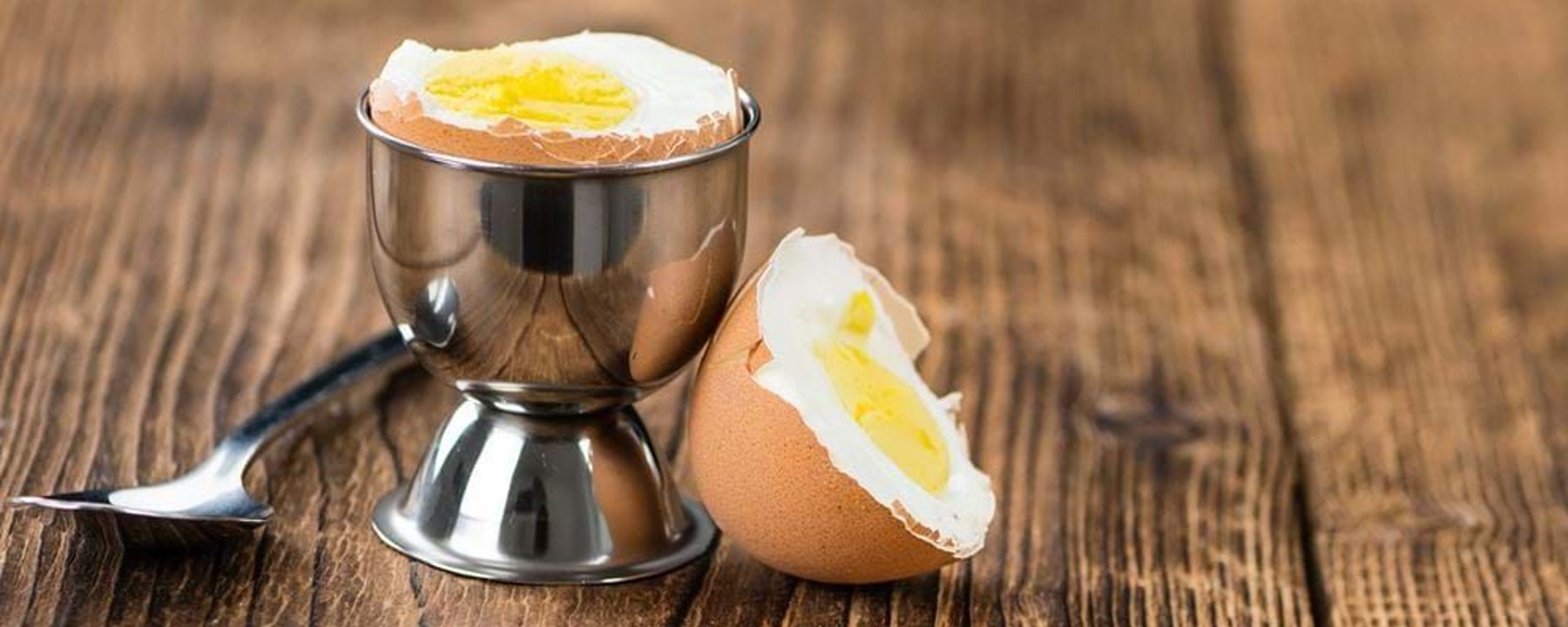 Soft boiled egg in a metal egg cup with a spoon on a wooden surface.