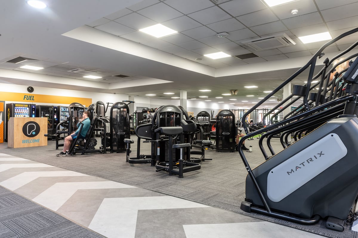 PureGym Woking: Rows of resistance machines, weight stacks, benches, and exercise balls in a brightly lit gym area.