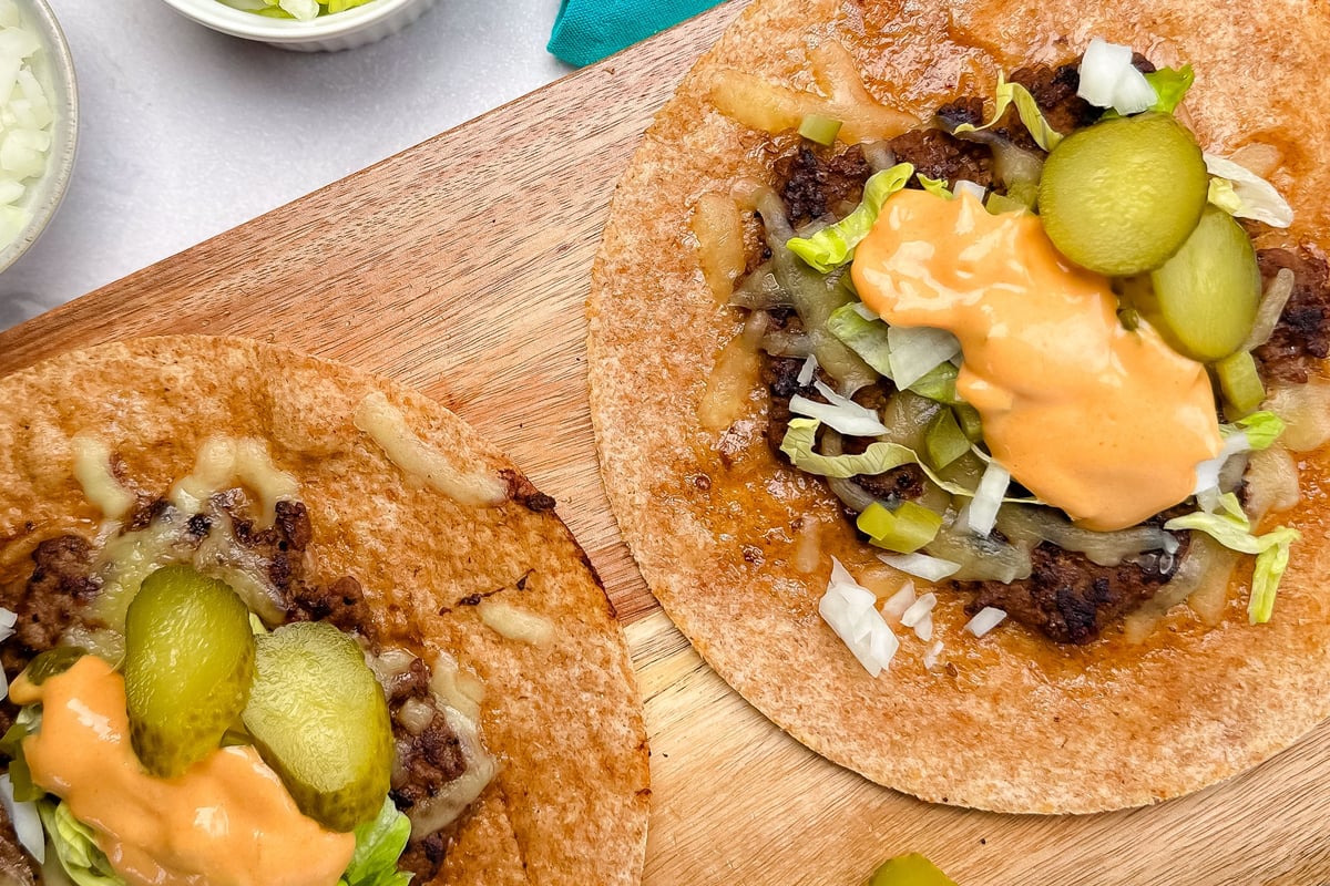 Two crispy tortillas filled with beef burgers, pickles, sauce and shredded lettuce