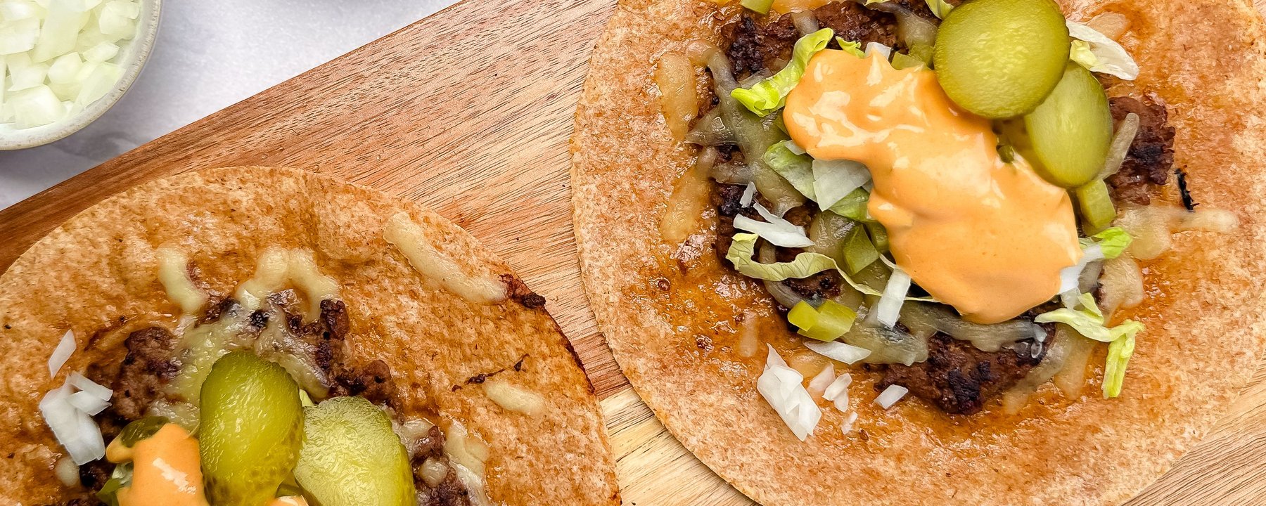 Two crispy tortillas filled with beef burgers, pickles, sauce and shredded lettuce