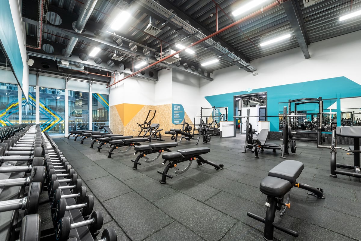 PureGym Manchester Spinningfields: Gym interior with rows of weight benches, free weights, and teal accent walls.