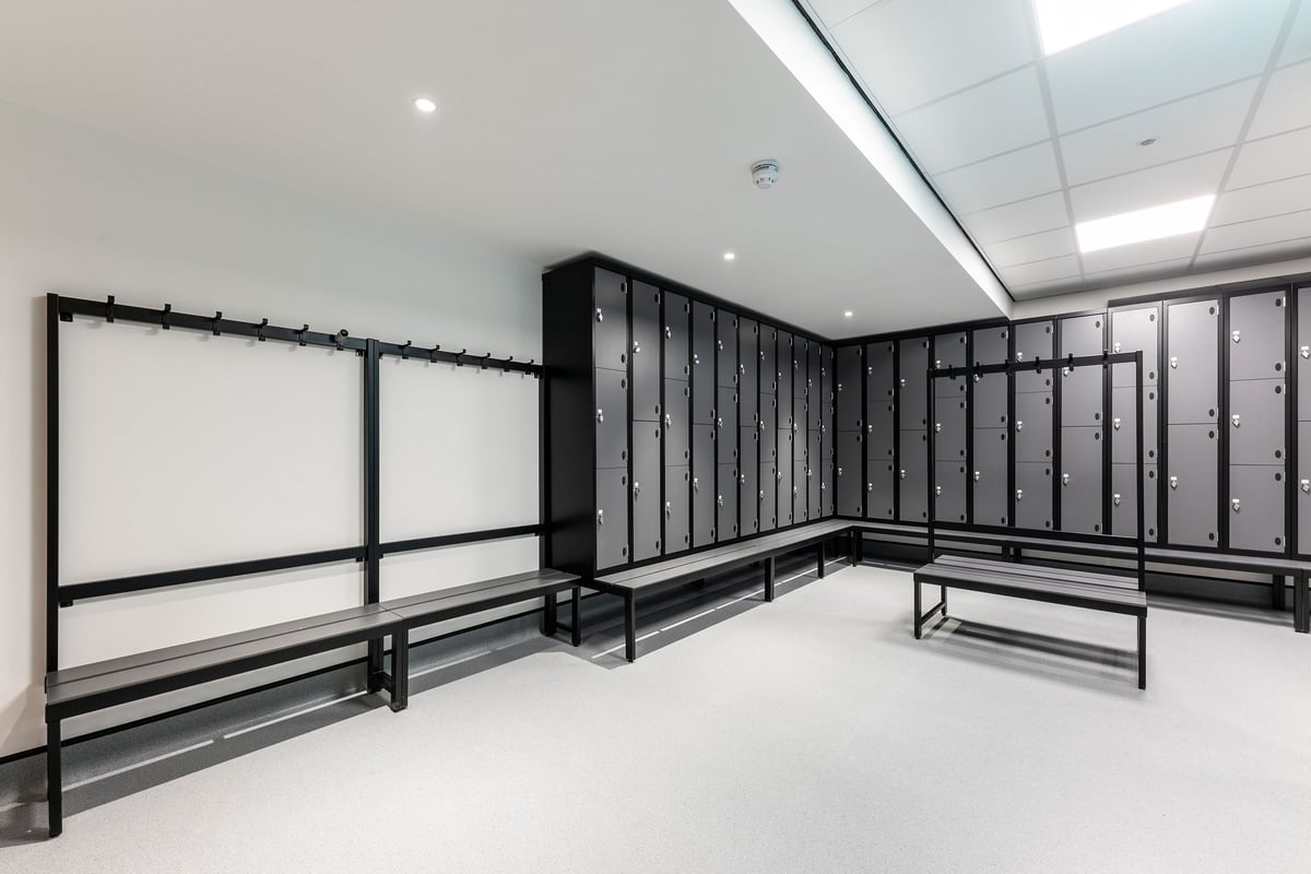 PureGym Manchester First Street: Lockers, benches, and rubberized flooring in changing room area.
