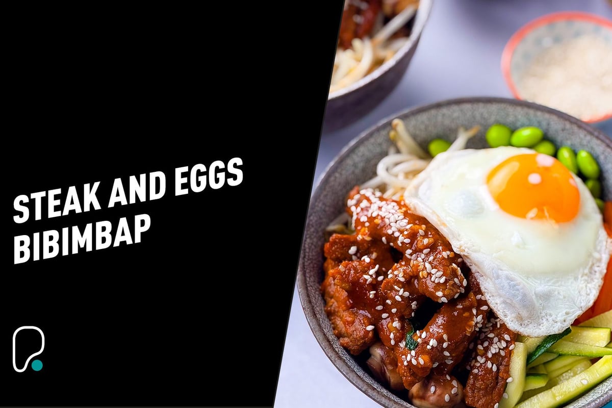 Bowl of bibimbap with fried egg, steak strips, edamame, carrots, and zucchini.