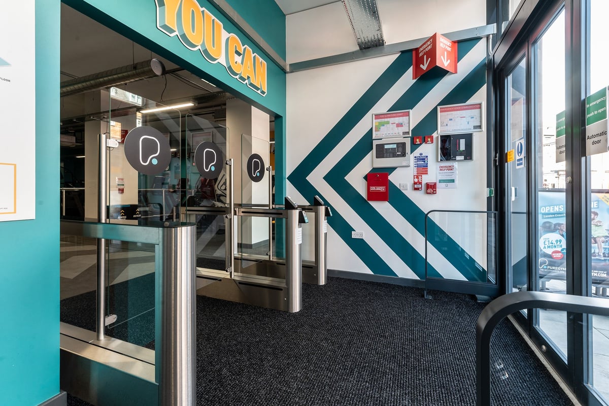 PureGym London Crouch End: Customer-facing lobby with self-service kiosks, glazed entrance, striped wall graphics.