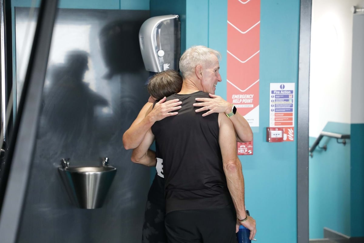 Two people hugging near a water fountain and emergency help point sign
