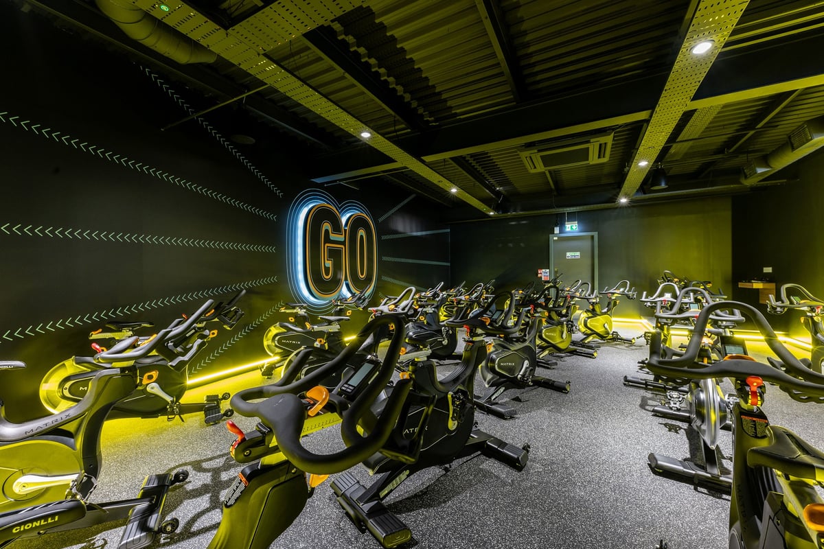 PureGym Glasgow Giffnock: Rows of stationary bikes, neon yellow and black colour scheme, motivational 'Go' sign on wall.
