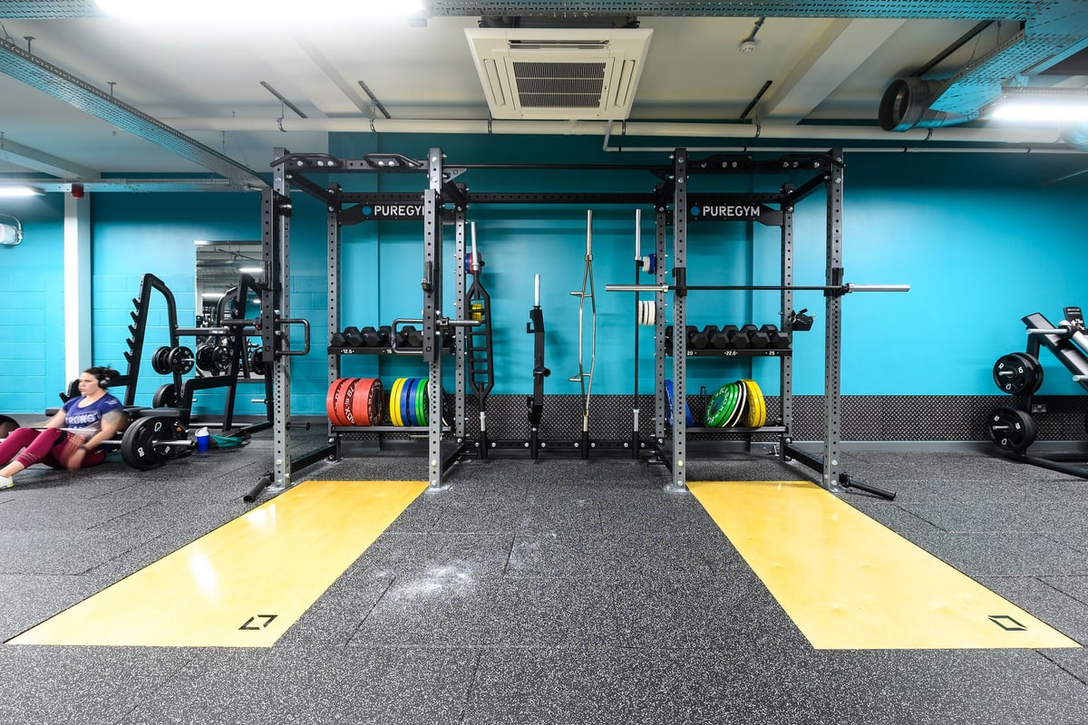 PureGym Salisbury: Squat racks, bumper plates, rubberized flooring in a teal and grey weightlifting studio.