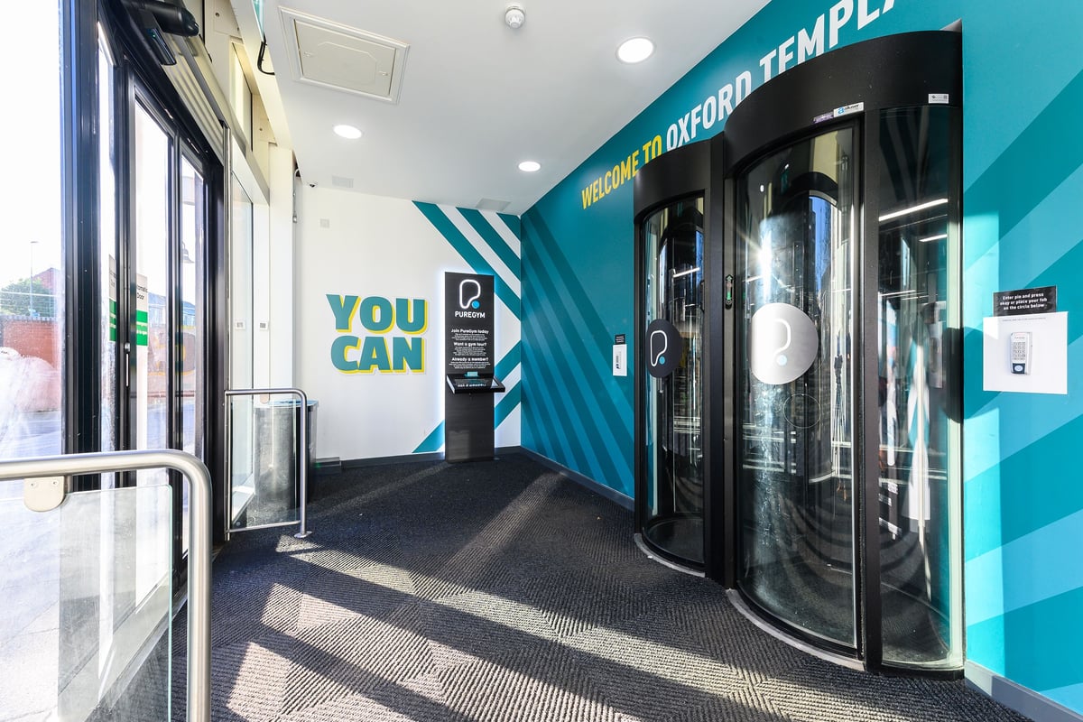 PureGym Oxford Templars Shopping Park: Entrance with revolving doors, turnstiles, and fitness equipment visible inside.