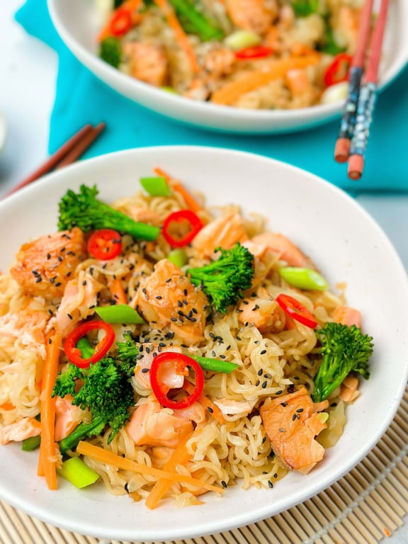Noodles with salmon, broccoli, carrot strips, red chili slices, and black sesame seeds in