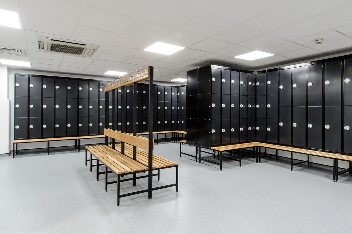 PureGym London Wembley: Rows of lockers, benches in an industrial changing room setting.