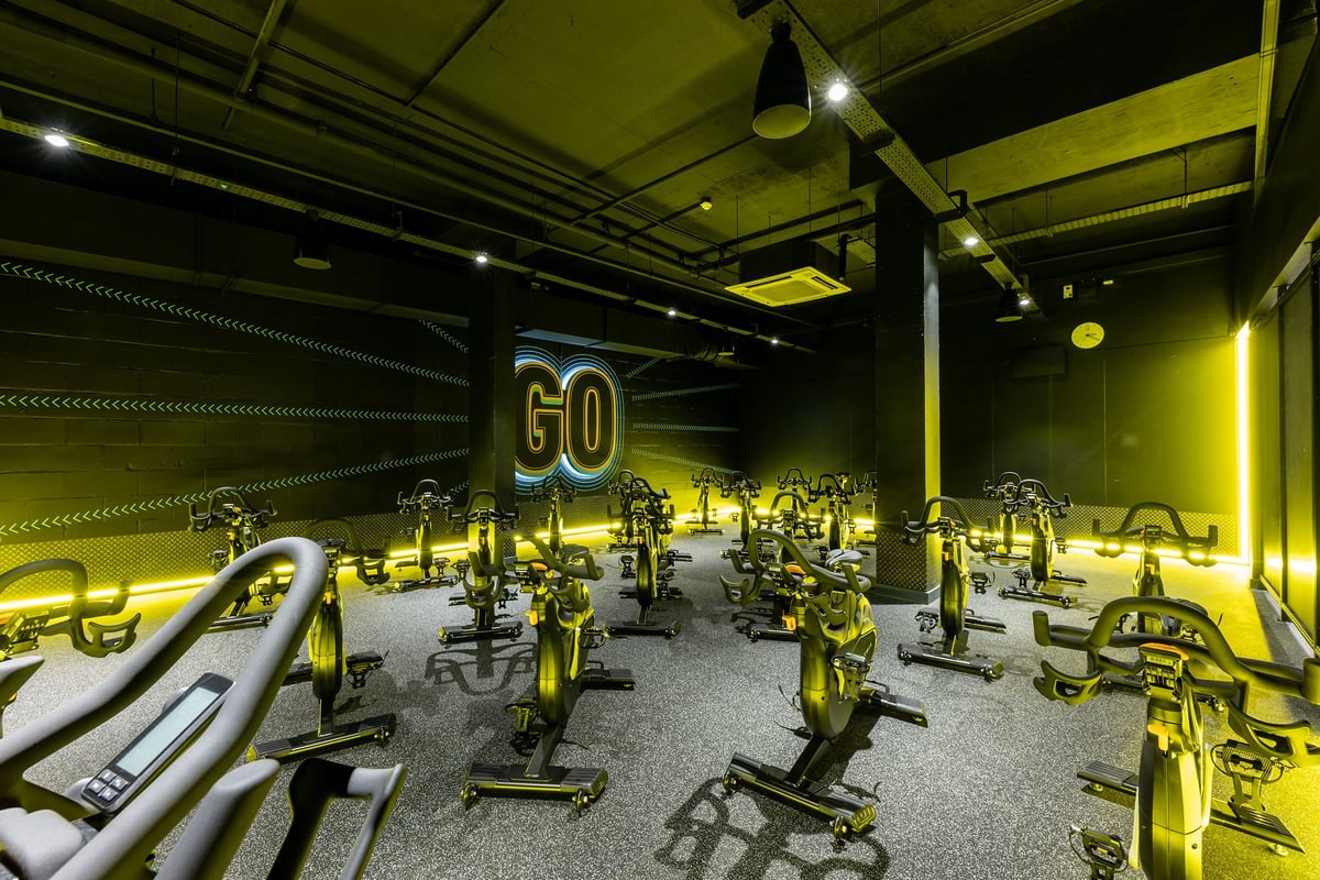 PureGym London Hammersmith Palais: Rows of stationary exercise bikes illuminated in a neon yellow lighting.