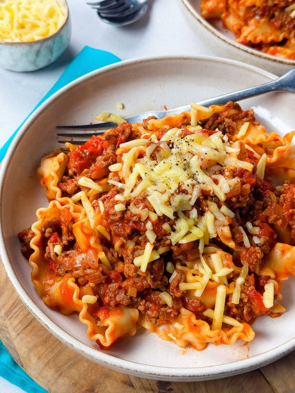 Pasta with meat sauce topped with grated cheese and black pepper on a beige plate.