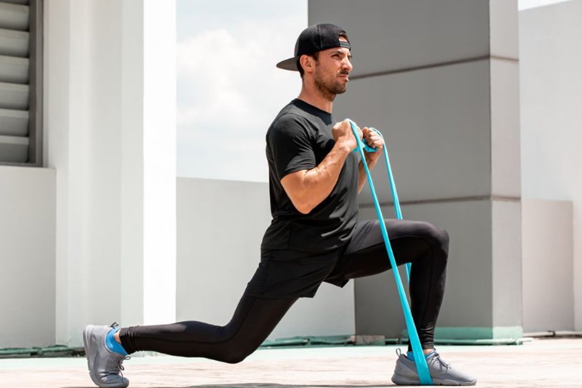 Mann führt Ausfallschritt mit Widerstandsband auf Dachterrasse durch.