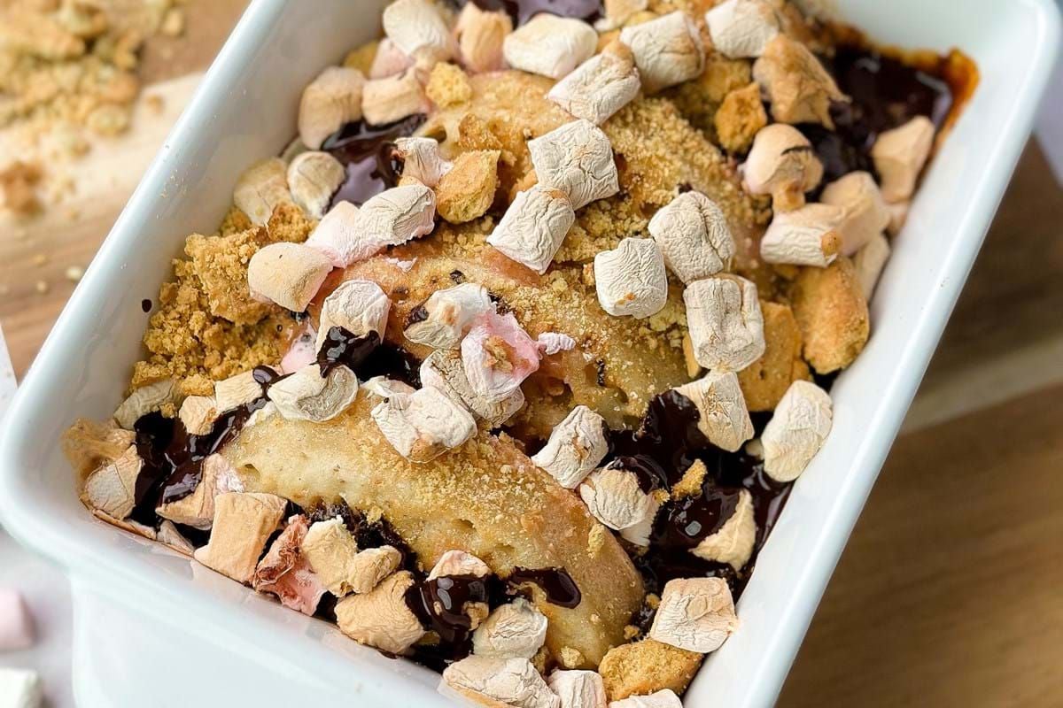 Baked dessert with marshmallows, chocolate sauce, and biscuit crumbs in a white dish