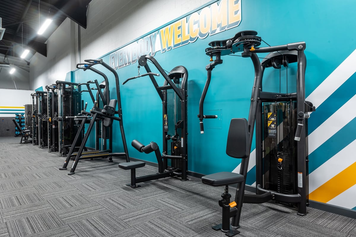PureGym Dungannon: Resistance machines, cable crossovers, benches, and a teal feature wall with "Welcome" signage.