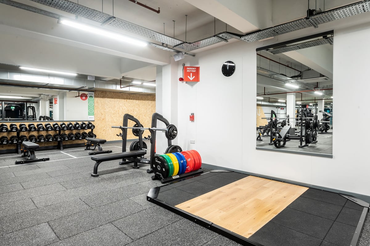 PureGym Gravesend: Weight benches, racks, plates, wooden platforms, and rubberized flooring in a fitness facility.