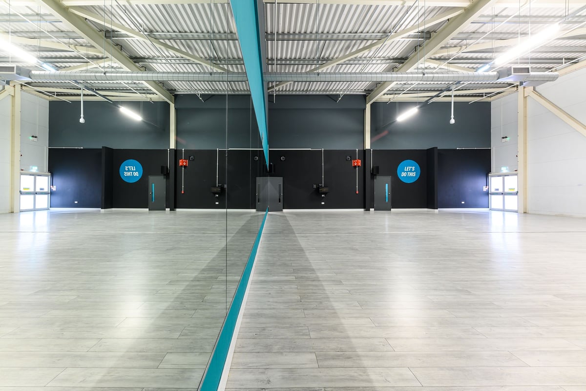 PureGym Wisbech: Teal and black studio spaces divided by mirrored walls, exercise equipment visible.