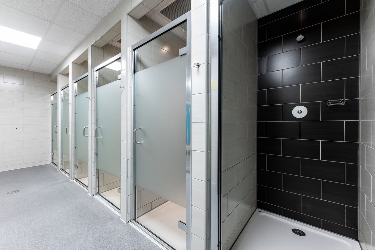 PureGym Ashton Under Lyne: Glass shower stalls and tiled walls in a changing room facility.