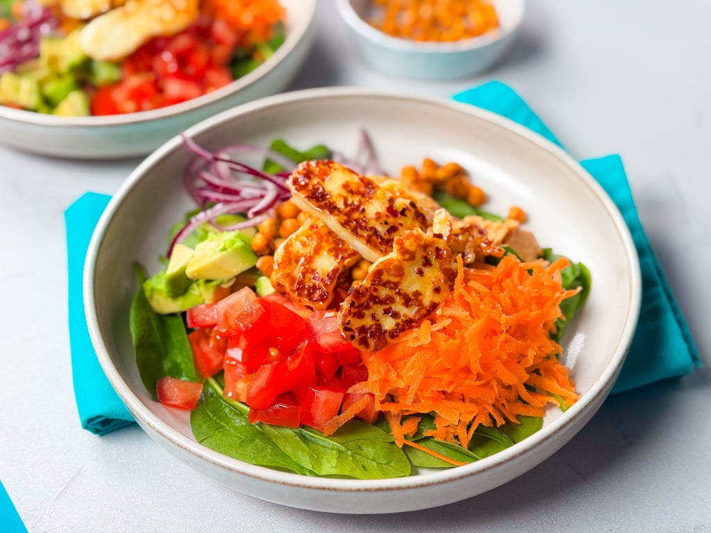 Bowl of salad with spinach, diced tomato, grated carrot, avocado, chickpeas, red onion