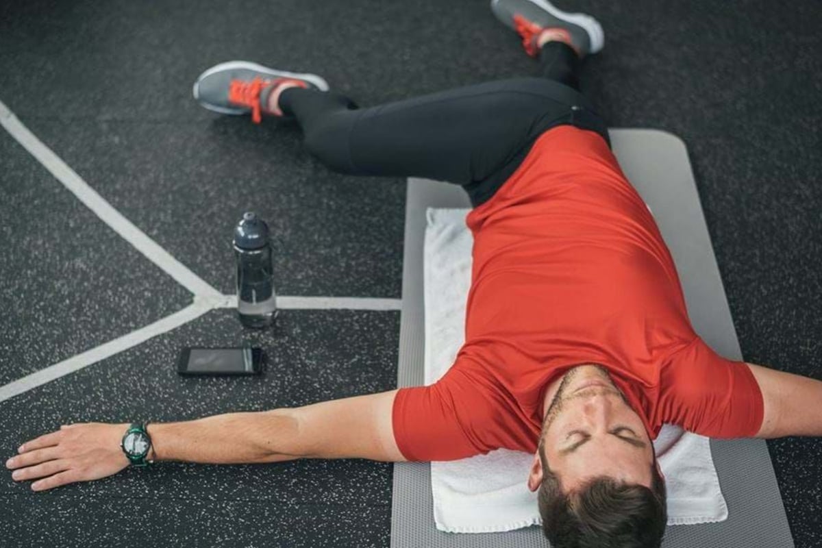 Man in red shirt stretching on mat with water bottle and phone nearby