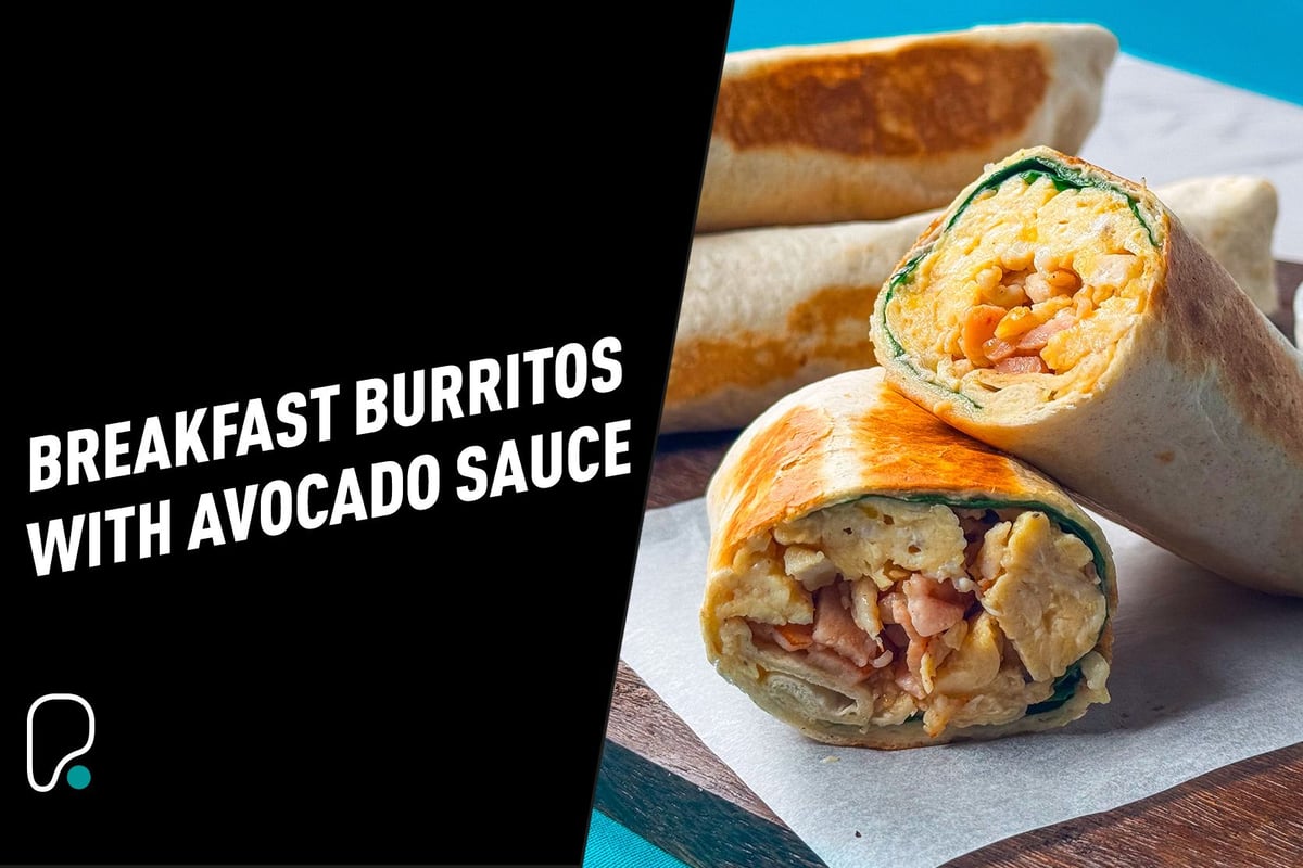 Two breakfast burritos cut in half showing scrambled eggs and bacon inside on a wooden board