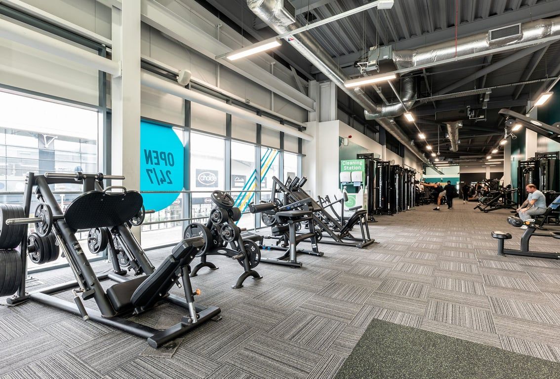 PureGym Chatham: Weight machines, leg presses, benches, and exposed piping on the ceiling in a gym setting.