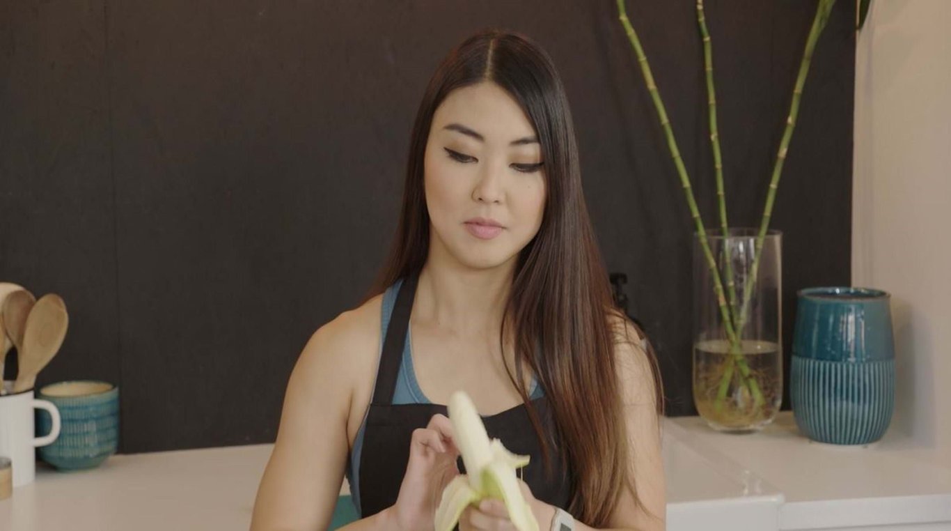 Woman peeling a banana in a kitchen with bamboo stalks in a glass vase behind her