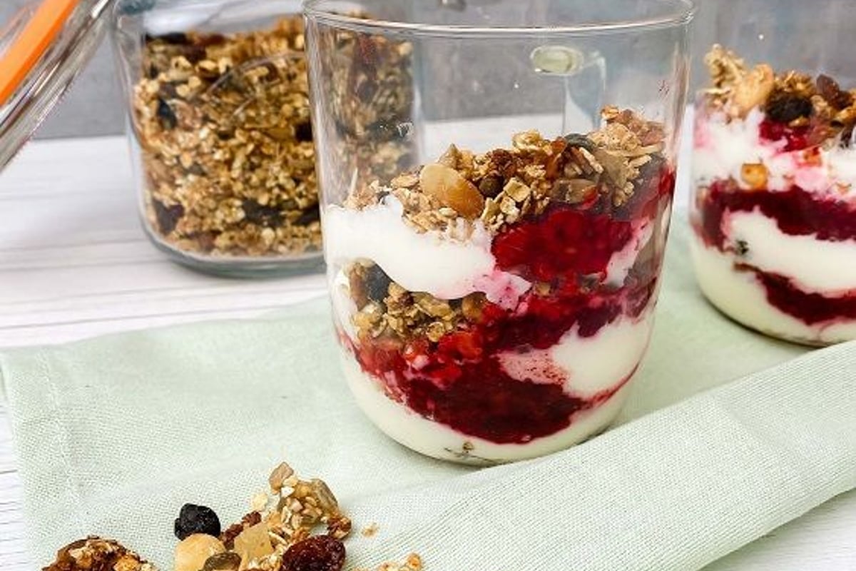 Two glasses with layered yoghurt, berry compote, and granola on a cloth