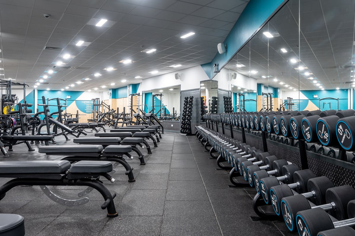 PureGym Aberdeen Kittybrewster: Rows of weight racks, free weights, benches, and aerobic steps in a brightly lit gym space.