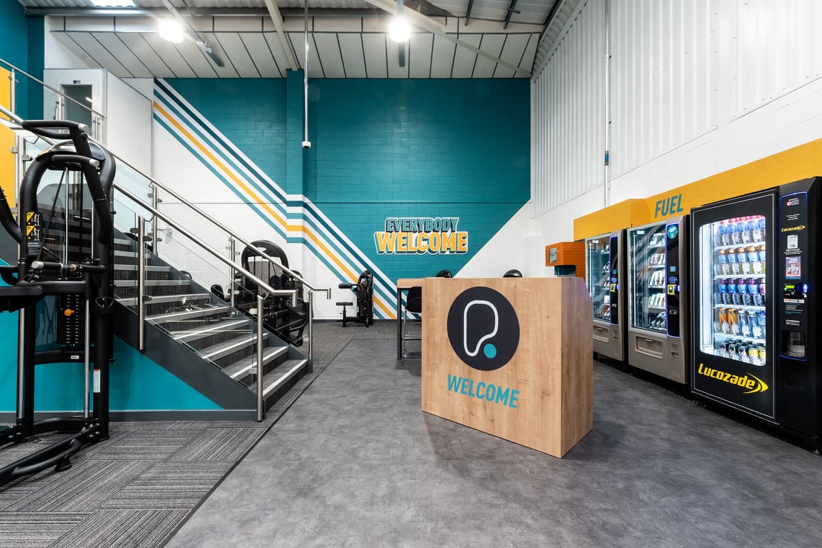PureGym Grantham Discovery Retail Park: Staircase, vending machines, reception desk area with industrial-style decor.