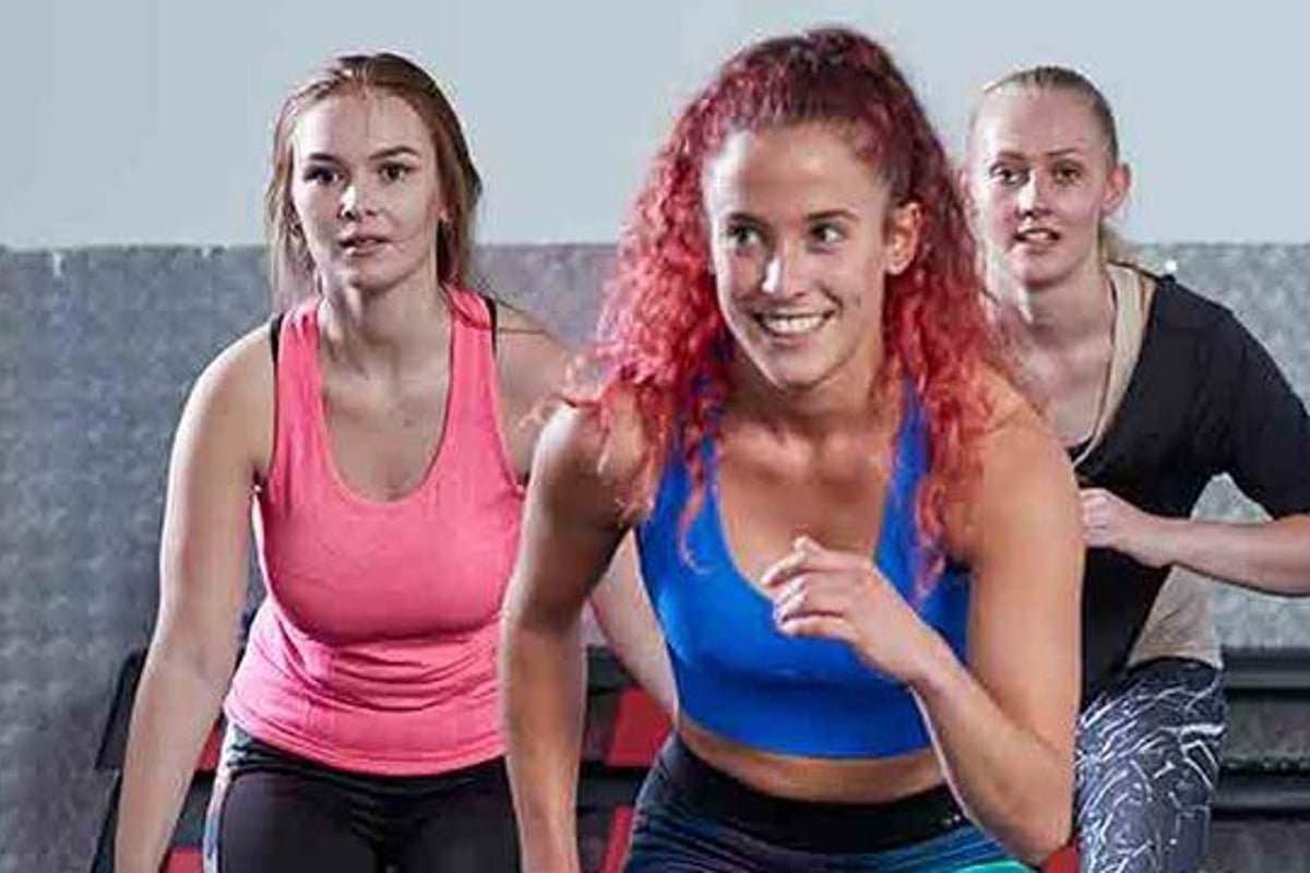 Drei Frauen in Sportkleidung trainieren zusammen in einem Fitnessstudio mit grauer struktu