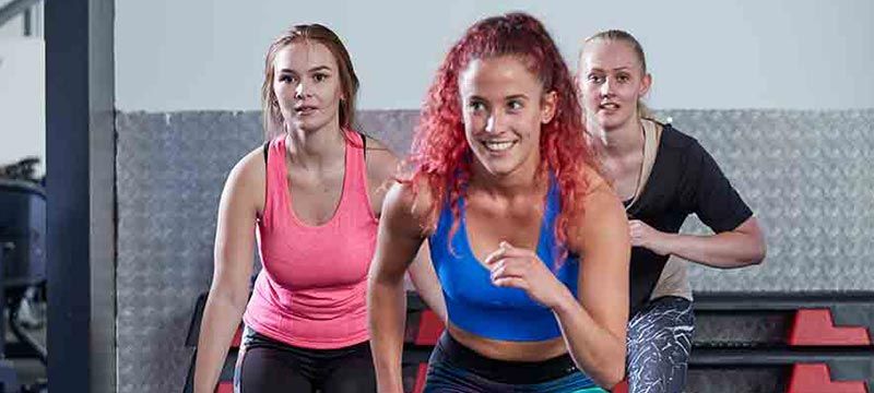 Drei Frauen in Sportkleidung trainieren zusammen in einem Fitnessstudio mit grauer struktu