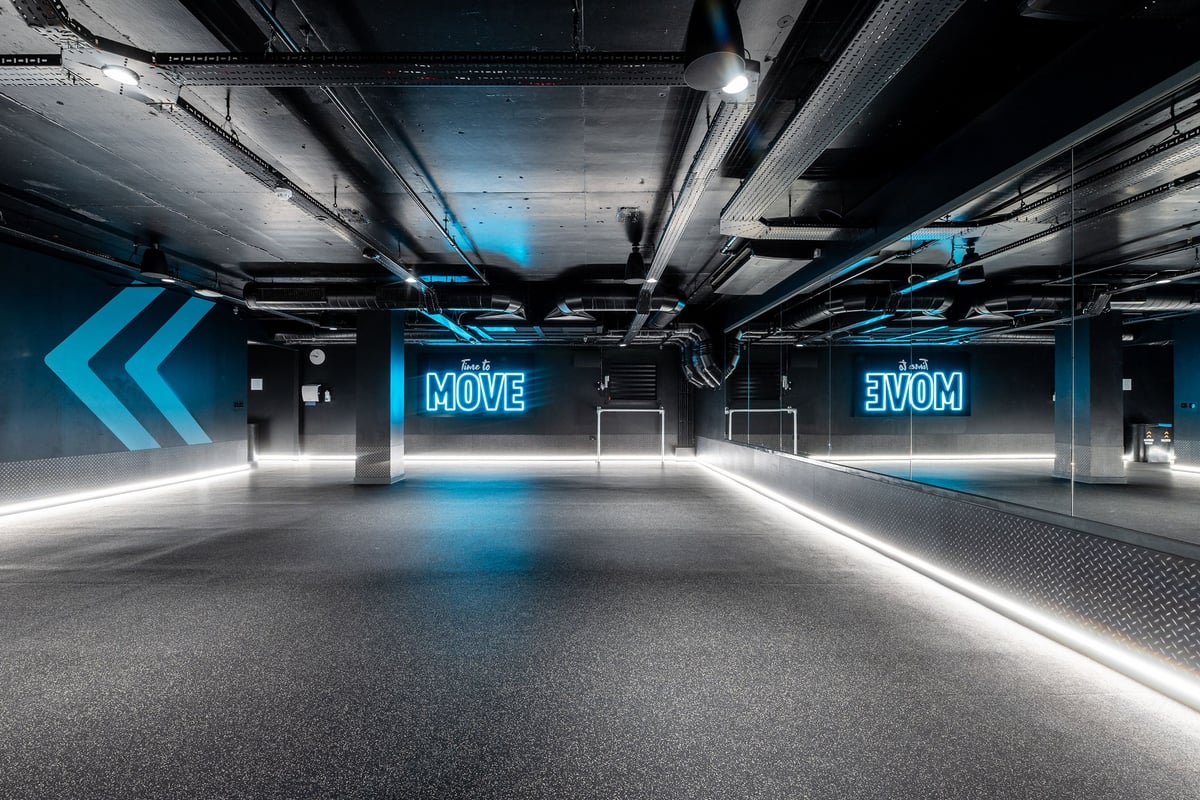 PureGym London Swiss Cottage: Futuristic gym studio with blue neon lights, mirrors, and open floor space.