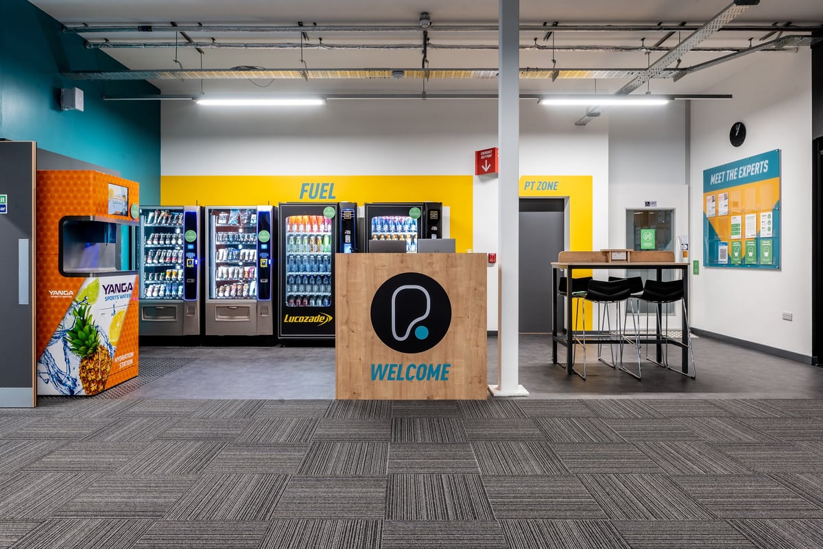 PureGym Bournemouth Mallard Road Retail Park: Vending machines, a welcome sign, and seating area in the entry lounge.