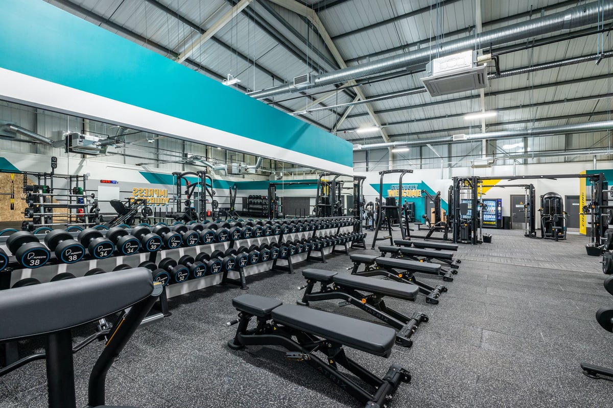 PureGym Oswestry: Rows of dumbbell racks, benches, weight plates, and resistance machines in a spacious gym facility.
