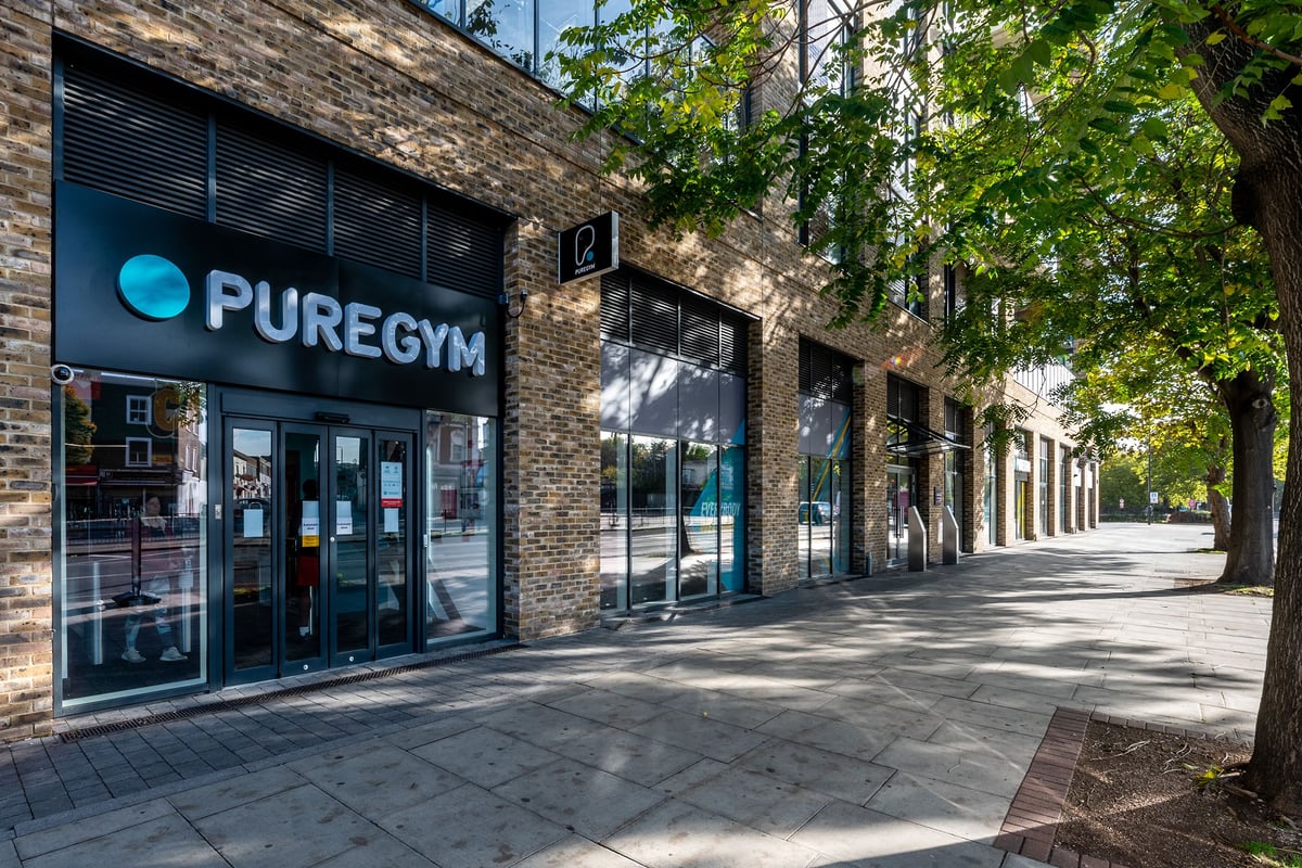 PureGym London Woolwich: Exterior view of a gym, with brick walls and large glass windows displaying the PureGym logo.