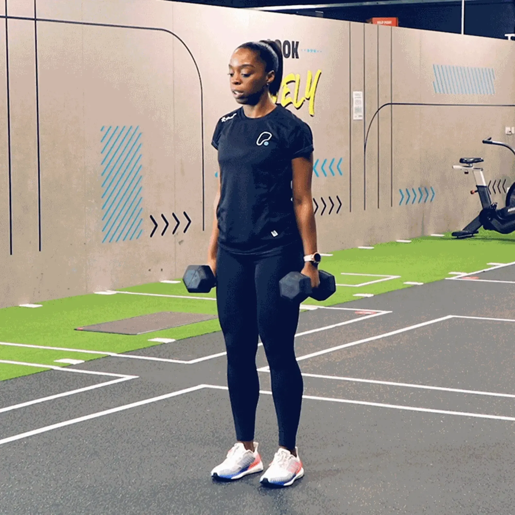 woman in black sportswear lifting dumbbells in a gym with green and grey flooring