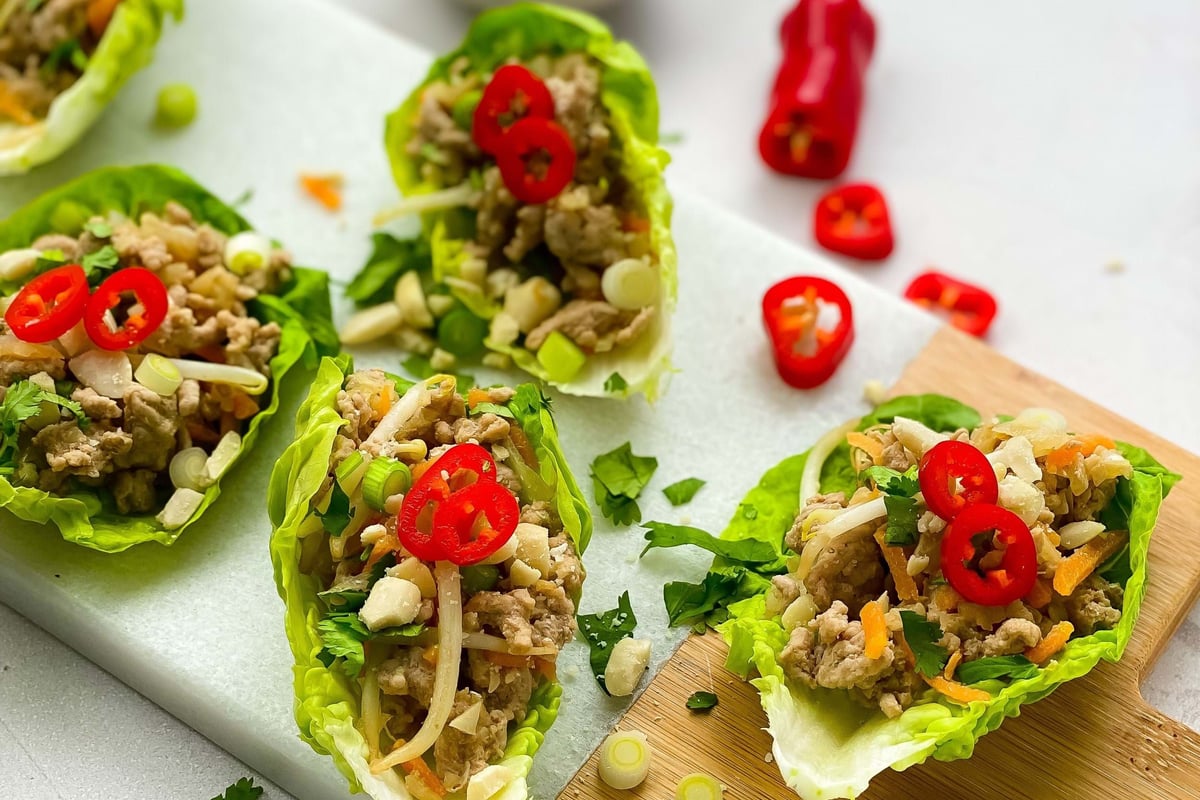 Lettuce cups filled with minced meat, chopped vegetables, and sliced red chili peppers.