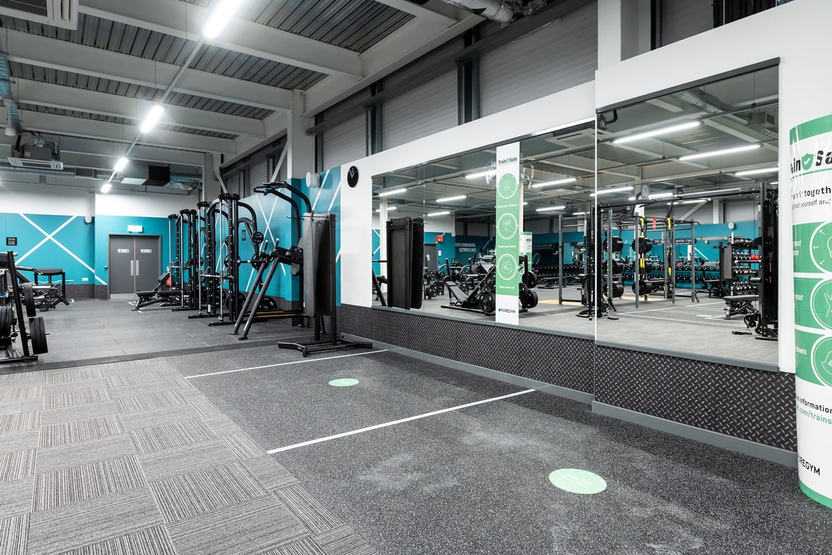 PureGym Andover: Fitness area with weight racks, cable machines, rubberized flooring, and teal accent walls.