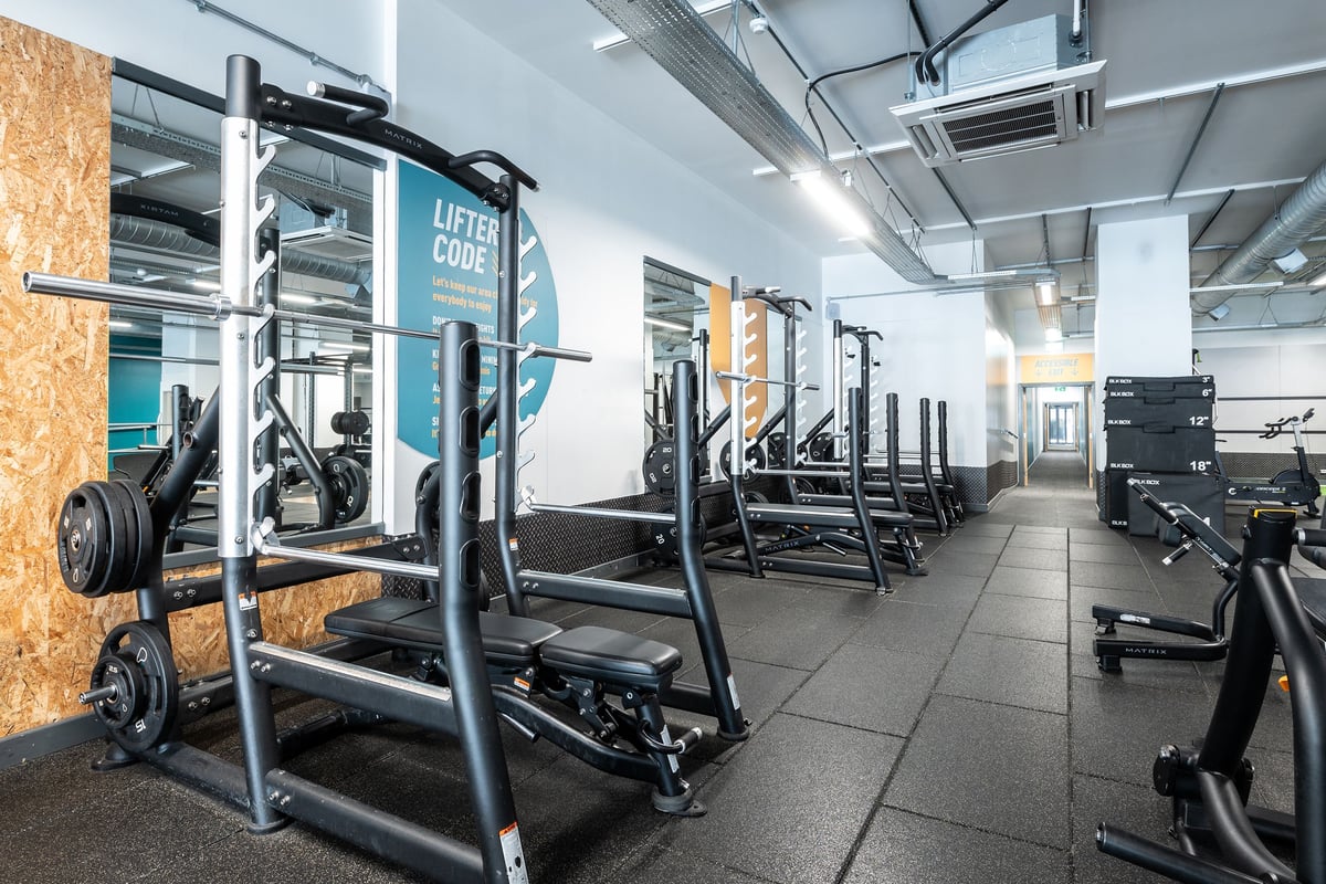 PureGym Stevenage: Squat racks, weight plates, benches, and rubberized flooring in a gym setting.