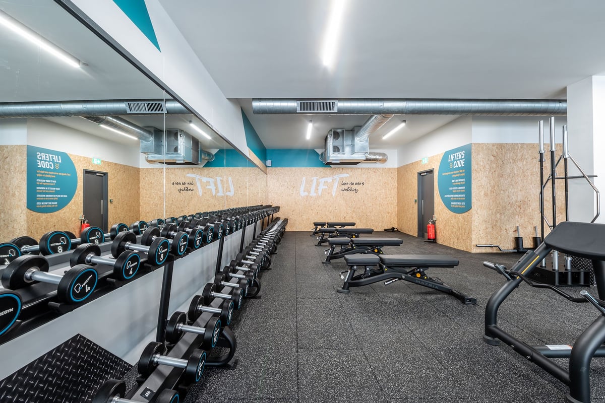 PureGym London Welling: Rows of stationary bikes, weight benches, and free weights in a gym space with teal accents.