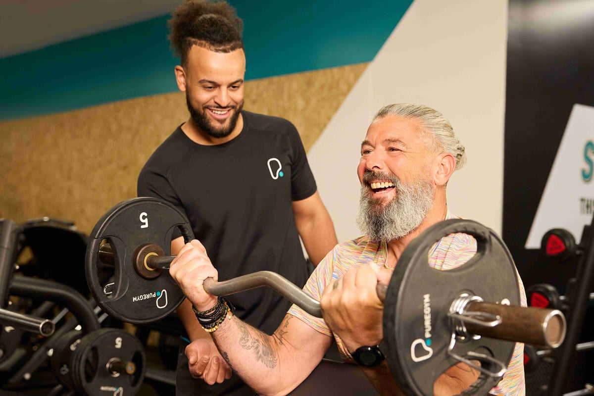 Man lifting barbell while trainer encourages him in gym setting